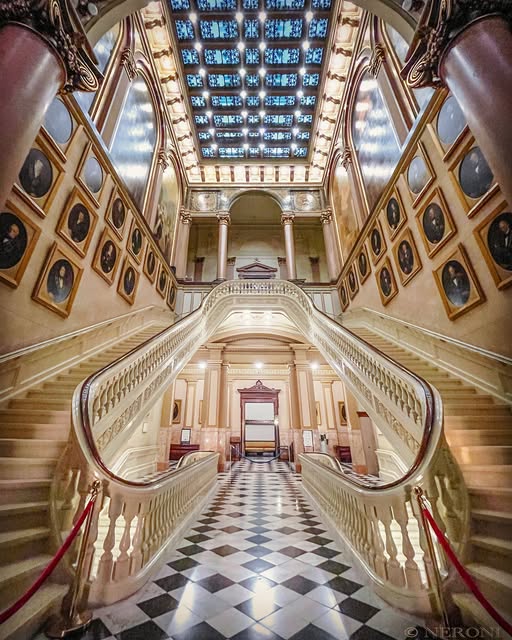 Grand marble staircase of a Masonic temple, lined with portraits of Past Masters beneath a stained glass ceiling